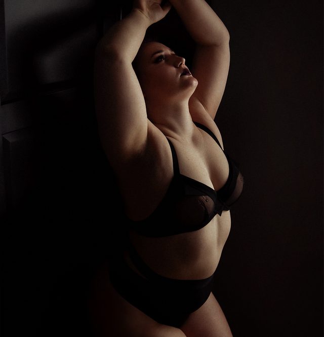Een vrouw gekleed in lingerie die tegen de muur aan leunt in een elegante pose.